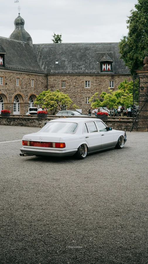 Weiße klassische Mercedes-Benz Limousine vor einer steinernen Schlossanlage